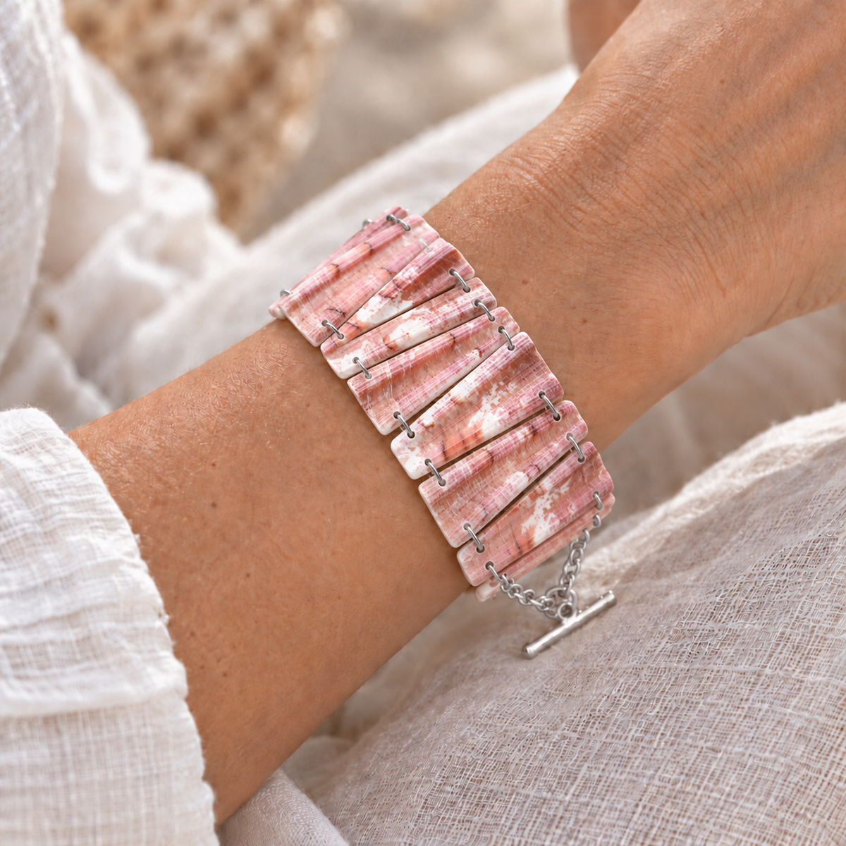 Bracelet en coquillage rose corail marbré de blanc porté au poignet, maillons trapèzes reliés par des anneaux argentés, fermoir en T argenté