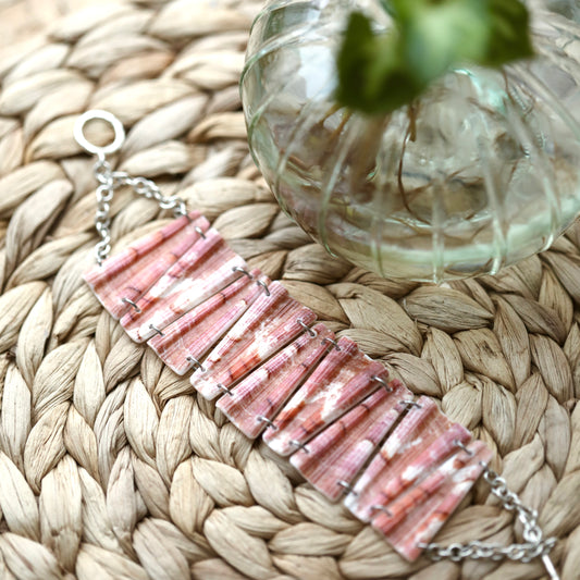 Bracelet entier en coquillage rose corail marbré de blanc, maillons trapèzes striés, chaîne et fermoir en T argentés, sur un set tressé
