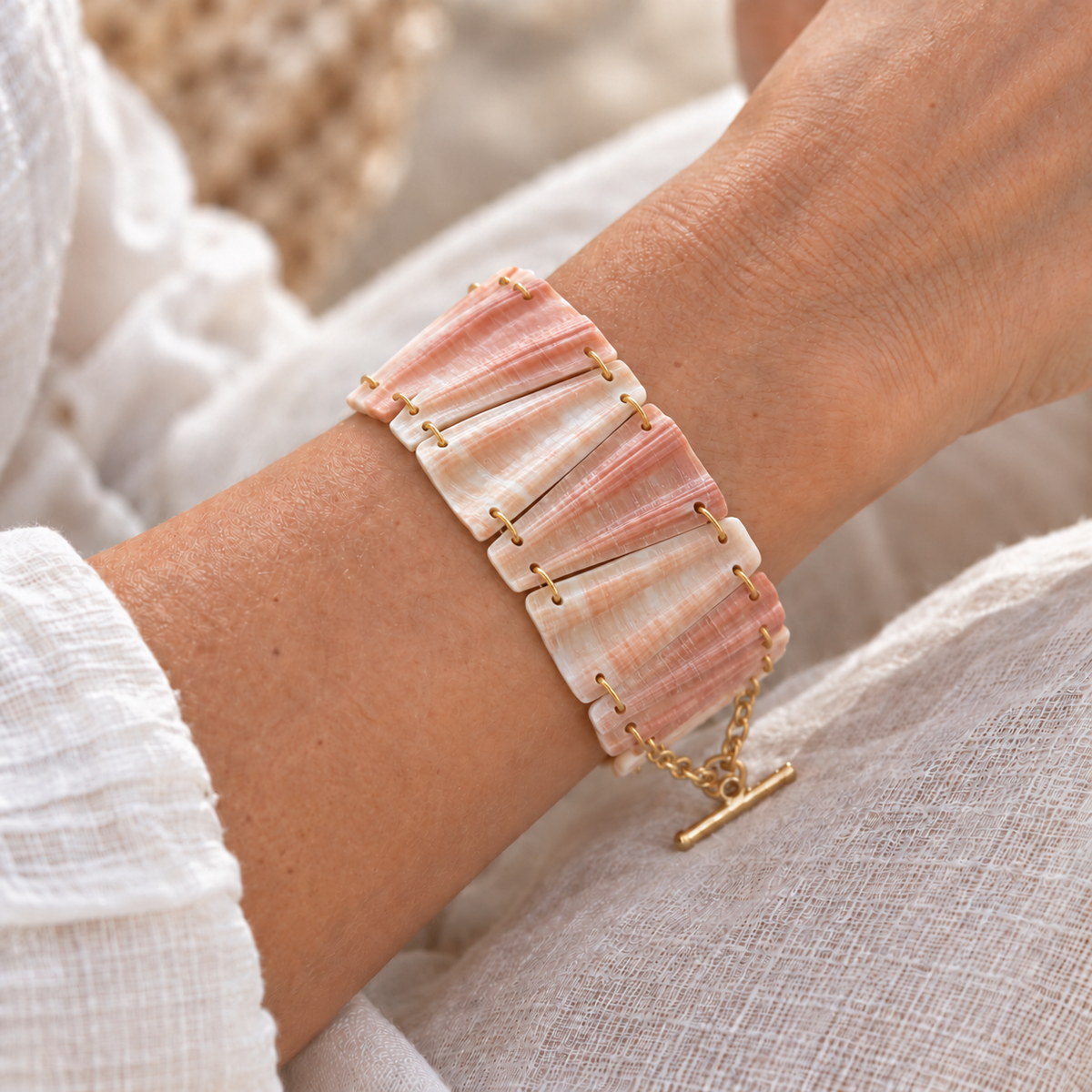 Bracelet en coquillage rose pêche et blanc porté au poignet, maillons trapèzes reliés par des anneaux dorés, fermoir en T doré