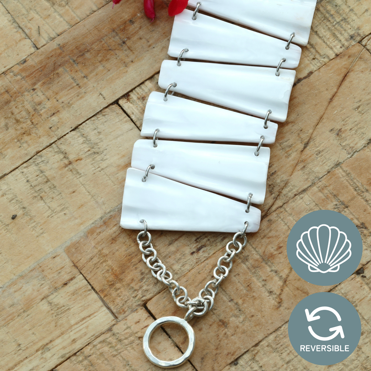 Face intérieure blanche d'un bracelet réversible en coquillage, maillons trapèzes reliés par une chaîne et un fermoir T, sur bois brut