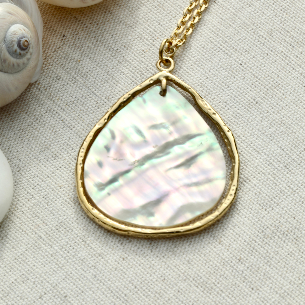 Gros plan sur les reflets irisés du pendentif nacre goutte doré. Atelier Sitaël